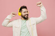 © ViDi Studio - Young smiling happy caucasian man 20s wearing trendy jacket shirt headphones listen to music dance have fun isolated on plain pastel light pink background studio portrait. People lifestyle concept
