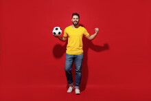 Full Size Body Length Young Bearded Man Football Fan In Yellow T-shirt Cheer Up Support Favorite Team Hold Soccer Ball Demonstrate Strength Power Isolated On Plain Dark Red Background Studio Portrait.