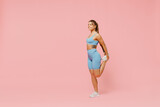 Fototapeta  - Full body young sporty athletic fitness trainer woman wear blue tracksuit spend time in home gym train do stretch legs exercise isolated on pastel plain light pink background. Workout sport concept.
