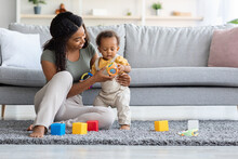 Caring Black Mom And Adorable Infant Son Playing With Toys At Home