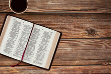 Open Holy Bible Book On Wooden Table Background With A Cup Of Coffee With Copy Space For Text. The Biblical Concept Of Reading And Studying The Scripture Given By God Jesus Christ. Top View.