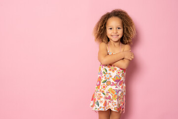 Cute little girl in summer dress with her hands folded standing over pink background.