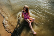 © Cavan Images - Young girl laying on lake shore in water