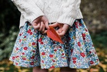 Child Holding A Red Leaf Behind Her Back Whilst Playing Outside