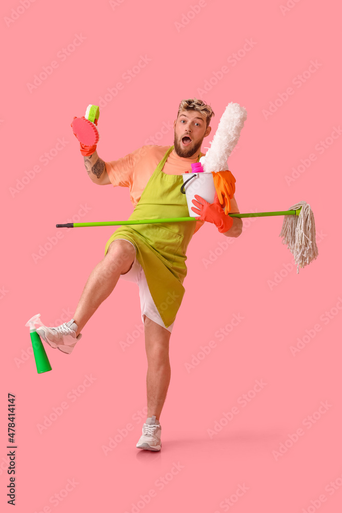 Shocked young man with cleaning supplies on pink background