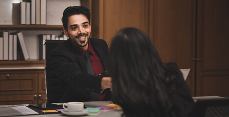 Closeup shot of Millennial Indian Asian professional successful executive bearded male businessman manager entrepreneur in formal suit sitting smiling shaking hands with businesswoman colleague