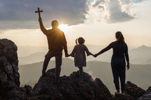 Silhouette Family Praying And Holding Christian Cross For Worshipping God On Mountain At Sunrise Background. Christian, Christianity, Religion Copy Space Background. Easter Sunday Concept:
