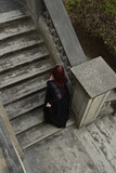 Fototapeta Młodzieżowe -  portrait of pretty  female model with red hair wearing glamorous gothic black lace ballgown.  Posing in a fairytale castle location with staircases 