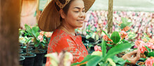 Asian Woman With Vietnamese Straw Hat Is Smiling And Holding Potted Flower In The Garden.