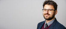 Portrait Of One Adult Caucasian Man 30 Years Old With Beard And Eyeglasses Looking To The Camera In Front Of White Wall Background Wearing Suit Young Businessman Success Concept Copy Space