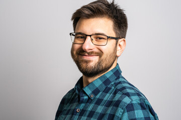 Portrait of one adult caucasian man 30 years old with beard and eyeglasses looking to the camera in front of white wall background smiling wearing casual shirt copy space