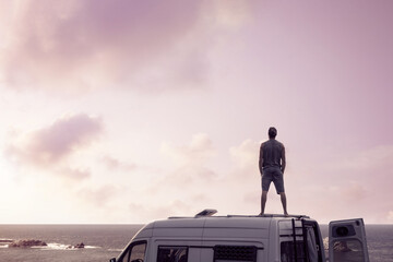 Wall Mural - Man standing on top of a camper van next to the ocean