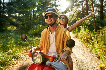 Smiling young caucasian couple riding scooter along road