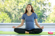 © Bangkok Click Studio - Caucasian millennial young happy female prenatal pregnant mother in casual outfit sitting crossed legs on yoga mat smiling closed eyes practicing meditation and exercise with dumbbell in living room