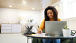 © Prostock-studio - Black woman sitting at desk, using pc writing in notebook