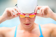 Female swimmer puts on goggles, wearing a white swimming cap and blue swimsuit
