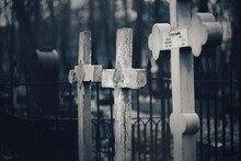 Three Old Stone Grave Crosses Are Behind A Dark Fence In The Cemetery In The Creepy Night Twilight. Horror. Religion.