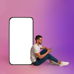 Poster - Cheery Arab guy sitting near big cellphone with blank screen, using mobile device, using new app in neon light, mockup