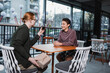 © LIGHTFIELD STUDIOS - Young man holding present near smiling girlfriend with wine in hotel cafe