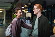 © LIGHTFIELD STUDIOS - Smiling man talking to girlfriend with backpack near reception in hotel