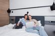 © LIGHTFIELD STUDIOS - Cheerful couple using laptop on bed in hotel room