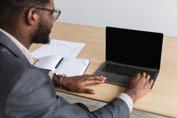 Millennial black entrepreneur working on laptop pc with blank screen at office, mockup for website