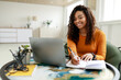 © Prostock-studio - Black woman sitting at desk, using pc writing in notebook