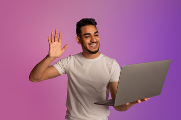 Poster - Portrait of young Arab guy waving at laptop, having video call on webcam, conferencing online in neon light