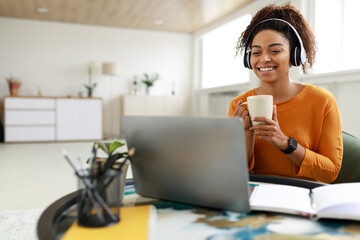 Canvas Print - Smiling black lady watching video on computer, drinking coffee