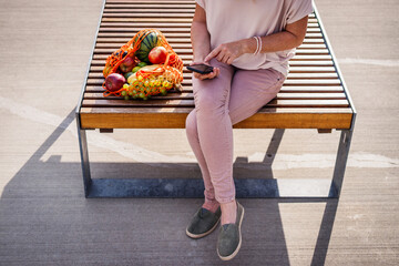 Wall Mural - Woman with reusable mesh bag sitting on bench and using smart phone in city. Resting at bench after shopping fruit in supermarket. Zero waste and plastic free concept
