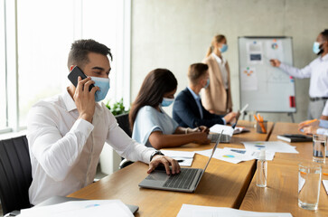 Poster - Arab Employee Wearing Mask Using Laptop And Cellphone During Meeting With Colleagues