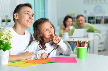 Wall Mural - Portrait of brother and sister sitting at table and spending time together