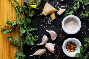 Wall Mural - Ingredients for the Italian traditional dish aglio olio e peperoncino with the addition of parsley and parmesan cheese on a black background, top view