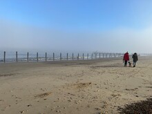 Beautiful Landscape With Female Couple Walking With Dog On Misty Environment On Sandy Beach At Happisburgh In Norfolk Coast In East Anglia Uk With Blue Skies After Fogbow On Bright Morning In December