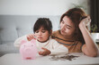 © FAMILY STOCK - Mother and daughter putting coins into piggy bank. Family budget and savings concept. Junior Savings Account concept