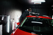 Car detailing concept. Man in face mask with orbital polisher in repair shop polishing roof of orange suv car.