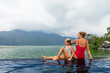 © Tropical studio - Happy family in Batur volcano hot spring spa. Travel in Kintamani, Bali. Mother, child chilling in infinity pool with lake view. Healthy lifestyle, recreational activity on summer holiday with kids