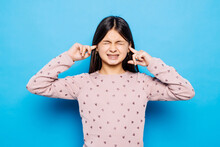 Stop Making This Annoying Sound. Unhappy Stressed Out Beautiful Caucasian Little Girl Wearing Blue T-shirt Over Blue Background Making Worry Face, Plugging Ears With Fingers, Irritated With Loud Noise