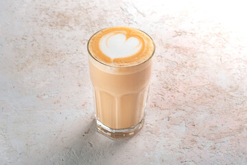 Big glass of cappuccino or latte with foam and a heart pattern on a stone white table. Coffee mug minimalist style