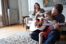 Mother Watching Father Teaching Daughter Playing Guitar In Living Room