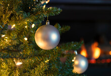 Single Silver Ball Ornament Hanging From Christmas Tree With Glowing Fireplace In Background