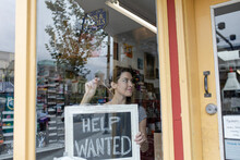Female Small Business Owner Placing Help Wanted Sign In Shop Window