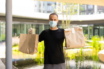 Wall Mural - Delivery guy with protective mask and gloves holding bag with groceries in front of a building.