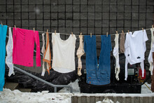 A Colorful Line Of Clothes Hanging Outside Air Drying With A Brick Building In The Background. The Line Has A Number Of Bras, Shirts, Jeans, And Tops. The Cloth Brassieres Are Of Large Sizes.
