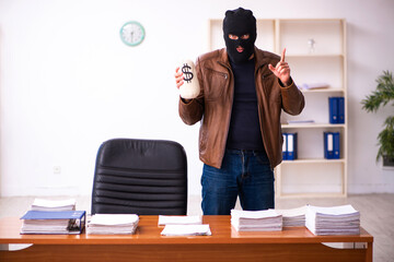 Young man in balaclava stealing information from the office