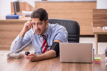 Young male employee suffering from hypertension at workplace