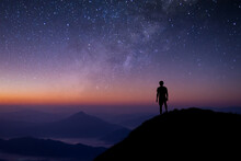 Silhouette Of Young Man Standing And Watched The Star, Milky Way And Night Sky Alone On Top Of The Mountain. He Enjoyed Traveling And Was Successful When He Reached The Summit.