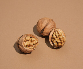 Few walnuts lie on pastel beige surface. Two nuts opened, one whole. Minimalist natural diversity and harvest.