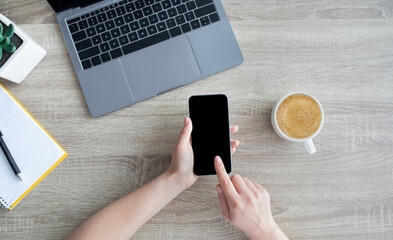 Aufkleber - Top view of female hands holding smartphone with blank screen, sitting at desk with laptop, coffee, notepad