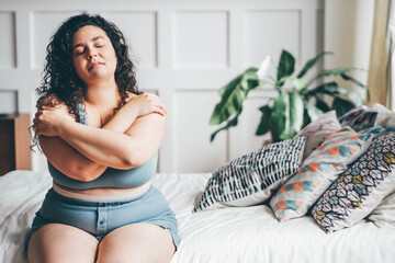 curly haired overweight young woman in grey top and shorts with satisfaction on face accepts curvy b